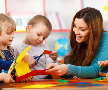 Woman assists preschool children with cutting paper